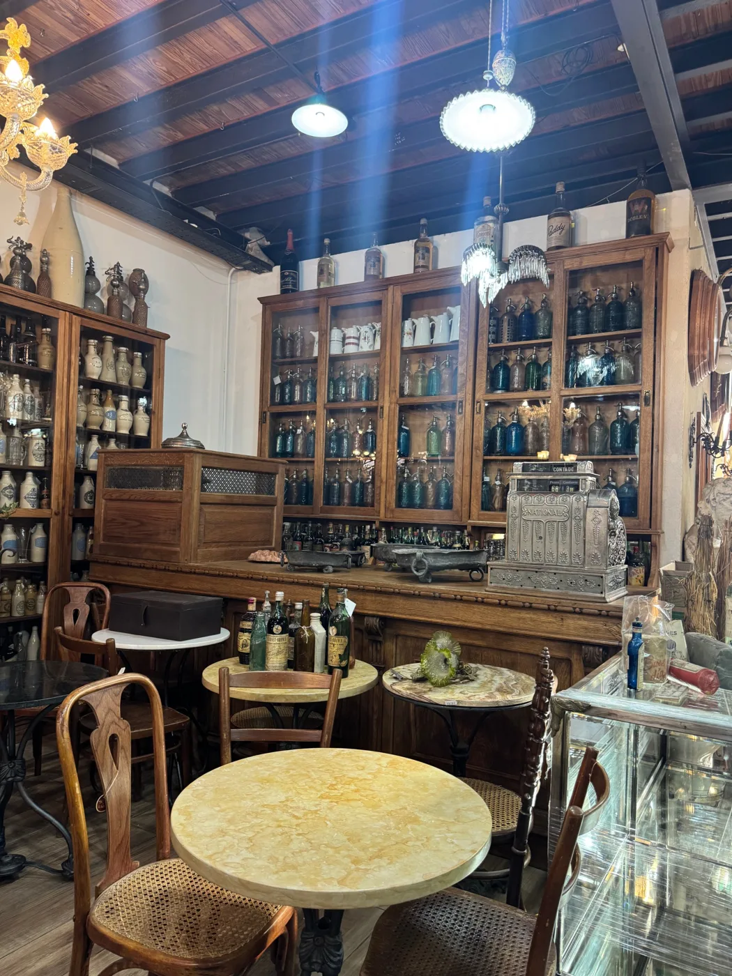 Salón de bar con mesas de mármol, caja registradora National y vitrinas con sifones