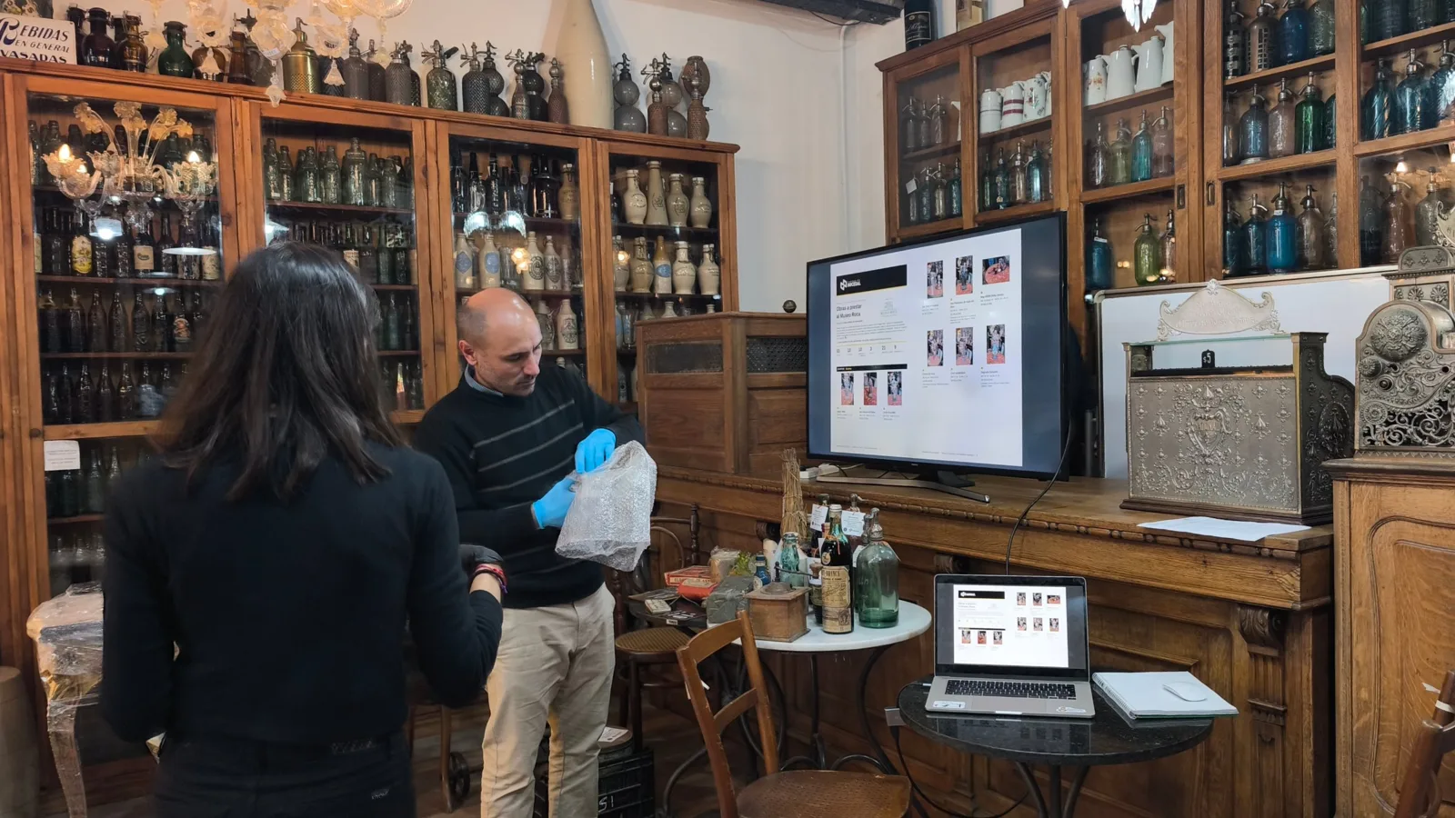 Embalaje de piezas de la Colección Nocedal con guantes y plástico de burbujas, junto a la pantalla con el inventario del préstamo
